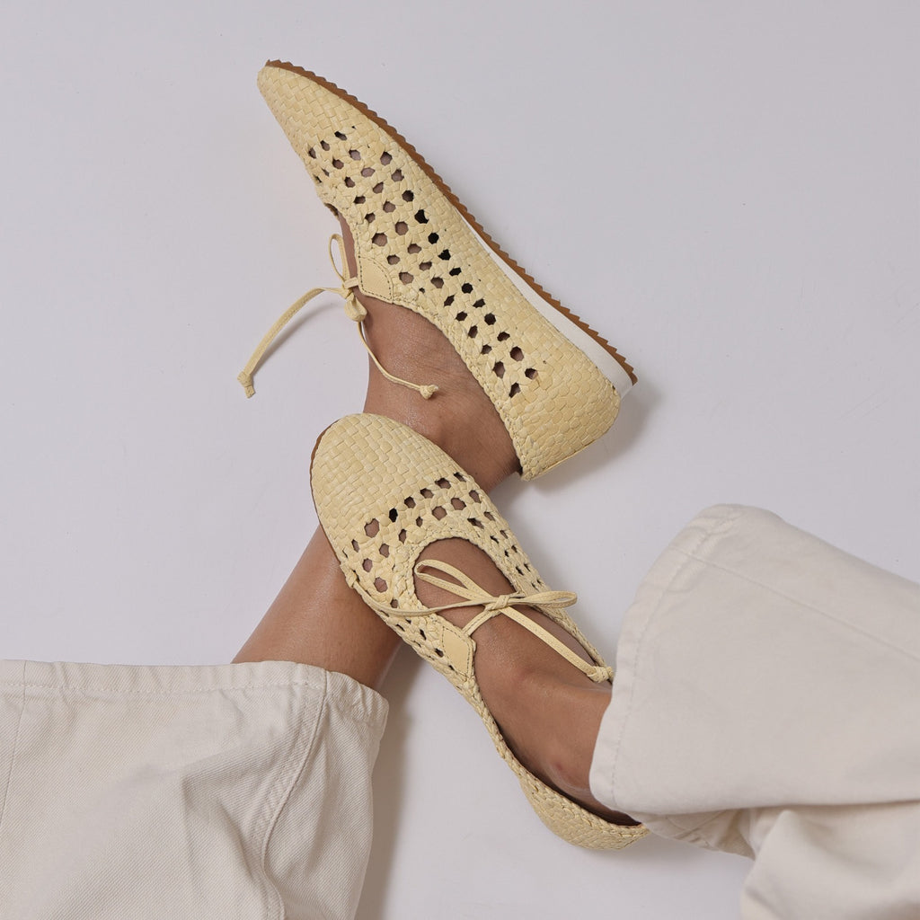 Beige woven shoes with ankle ties worn by a person on a light gray background